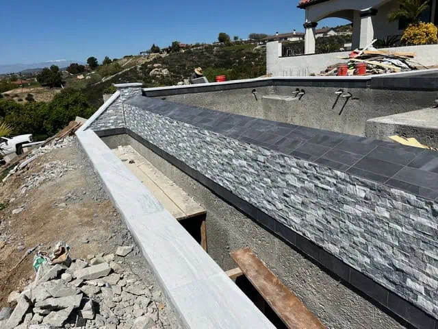 Backyard pool construction with stone veneer and modern design elements.