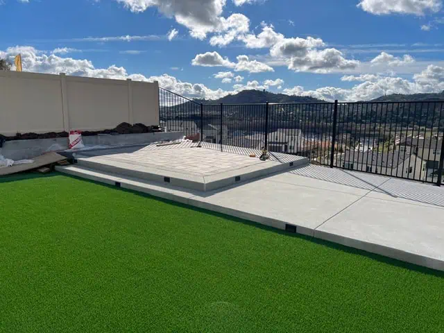 Rooftop deck featuring artificial grass, concrete flooring, and safety railing for outdoor relaxatio.