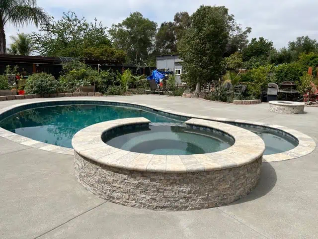 Pool and hot tub renovation with stone accents in a landscaped backyard.