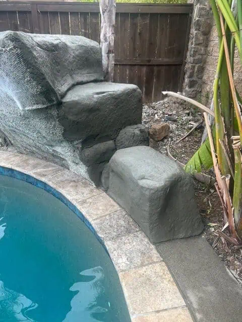Waterfall feature with large rocks in a backyard pool area.
