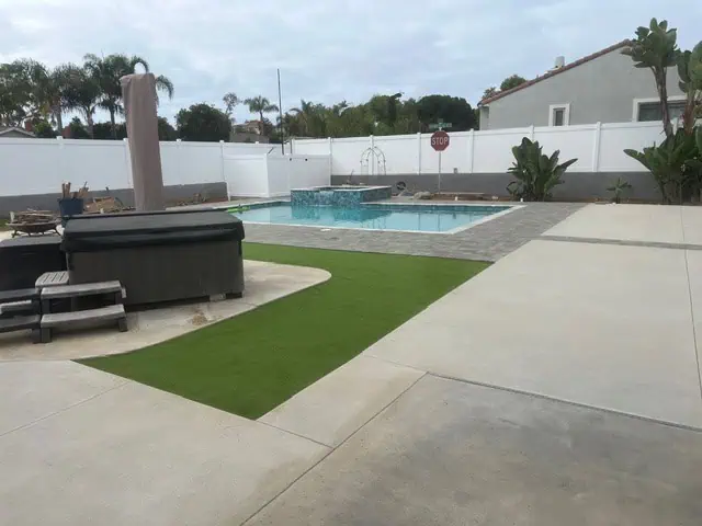 Backyard pool with spa, artificial grass, and modern concrete patio for outdoor relaxation.
