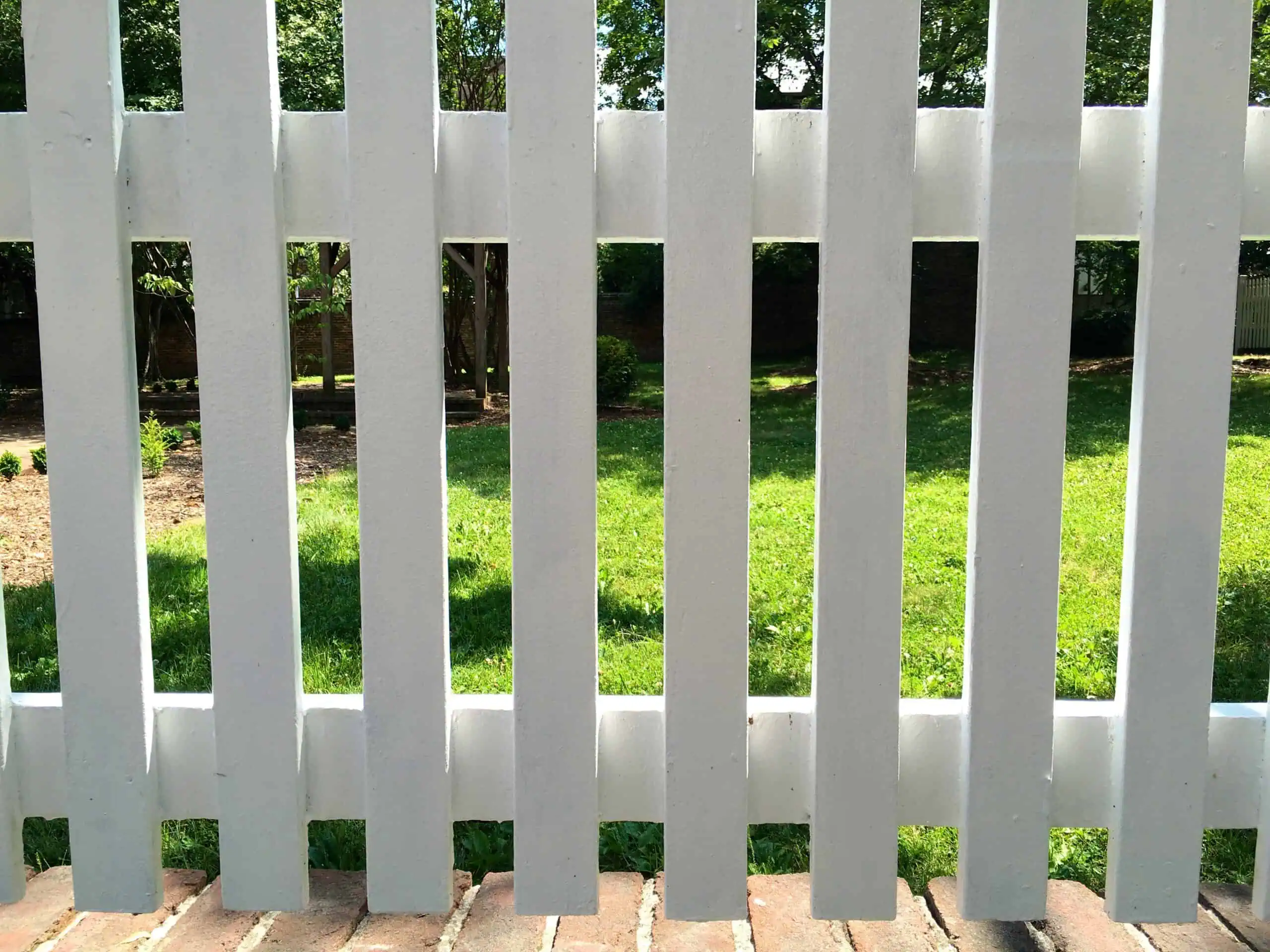 Fence with vertical white slats in a backyard setting.